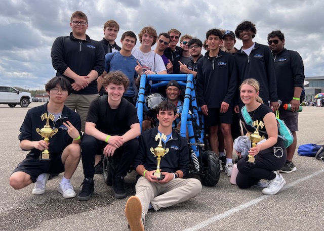 students gather around an electric vehicle with trophies