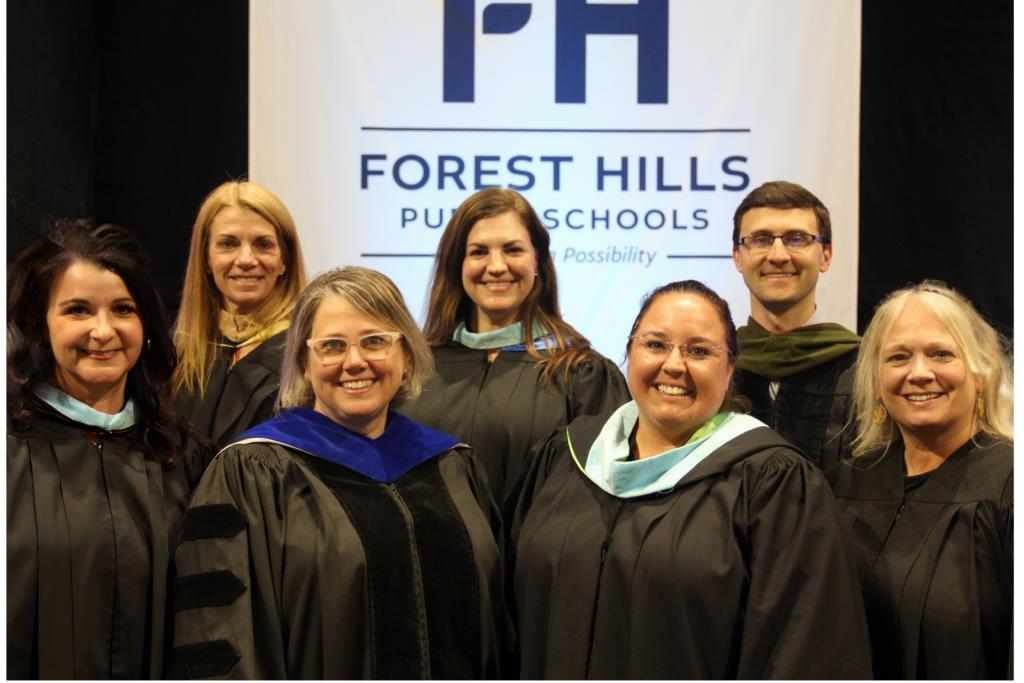 seven adults in commencement regalia stand in front of an FHPS banner, these are the seven adults on the FHPS board of education
