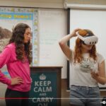 two girls in a high school classroom and one girl has a virtual reality headset on