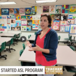 A clip for from the news story: a woman with brown hair pulled up wearing a red tshirt and navy blue cardigan stands in a high school classroom talking about ASL