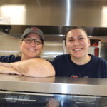 Two lunch staff professionals in a school kitchen.